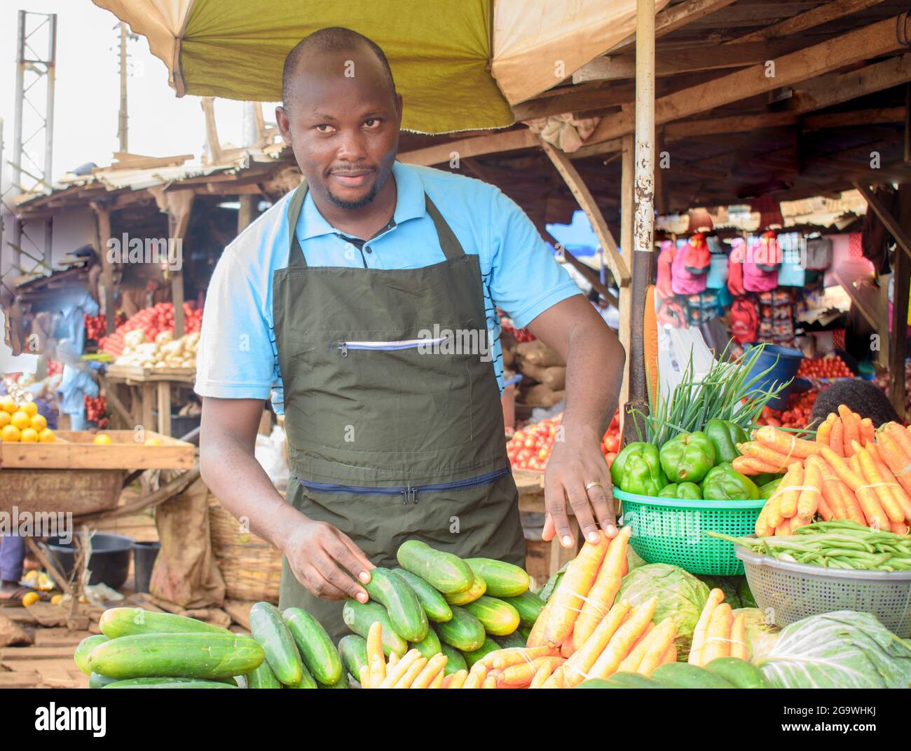 Photo de stock d'un homme d'alimentation africain ou d'un homme d'affaires avec un tablier, debout à sa stalle dans un marché, prêt à vendre à des clients Banque D'Images