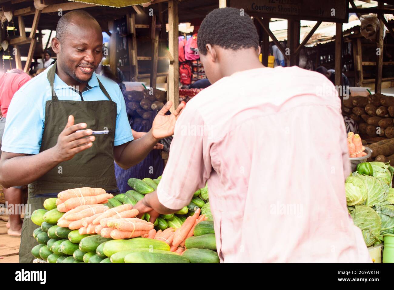 Photo de stock d'un homme d'alimentation africain ou d'un homme d'affaires avec un tablier, debout à sa stalle dans un marché, prêt à vendre à des clients Banque D'Images