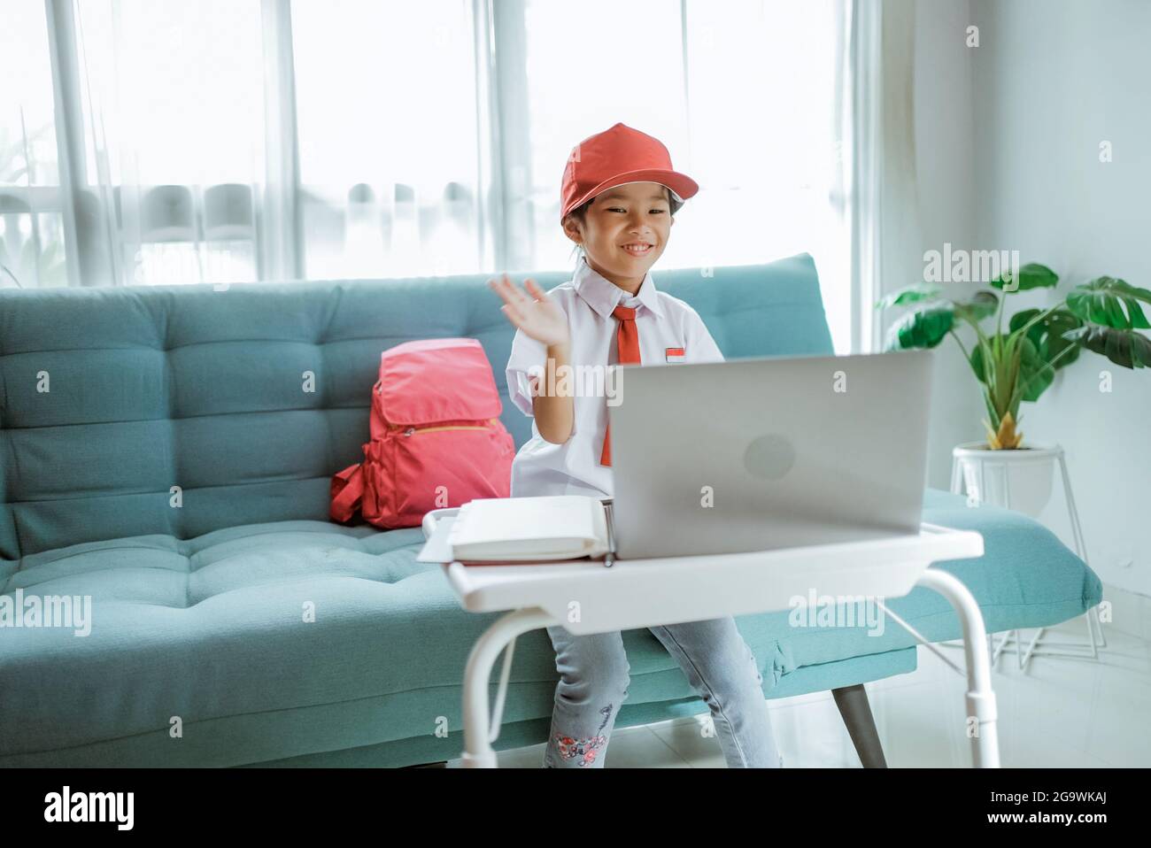 élève de l'école primaire avec uniforme agitant à son professeur et ami pendant la session de classe en ligne Banque D'Images