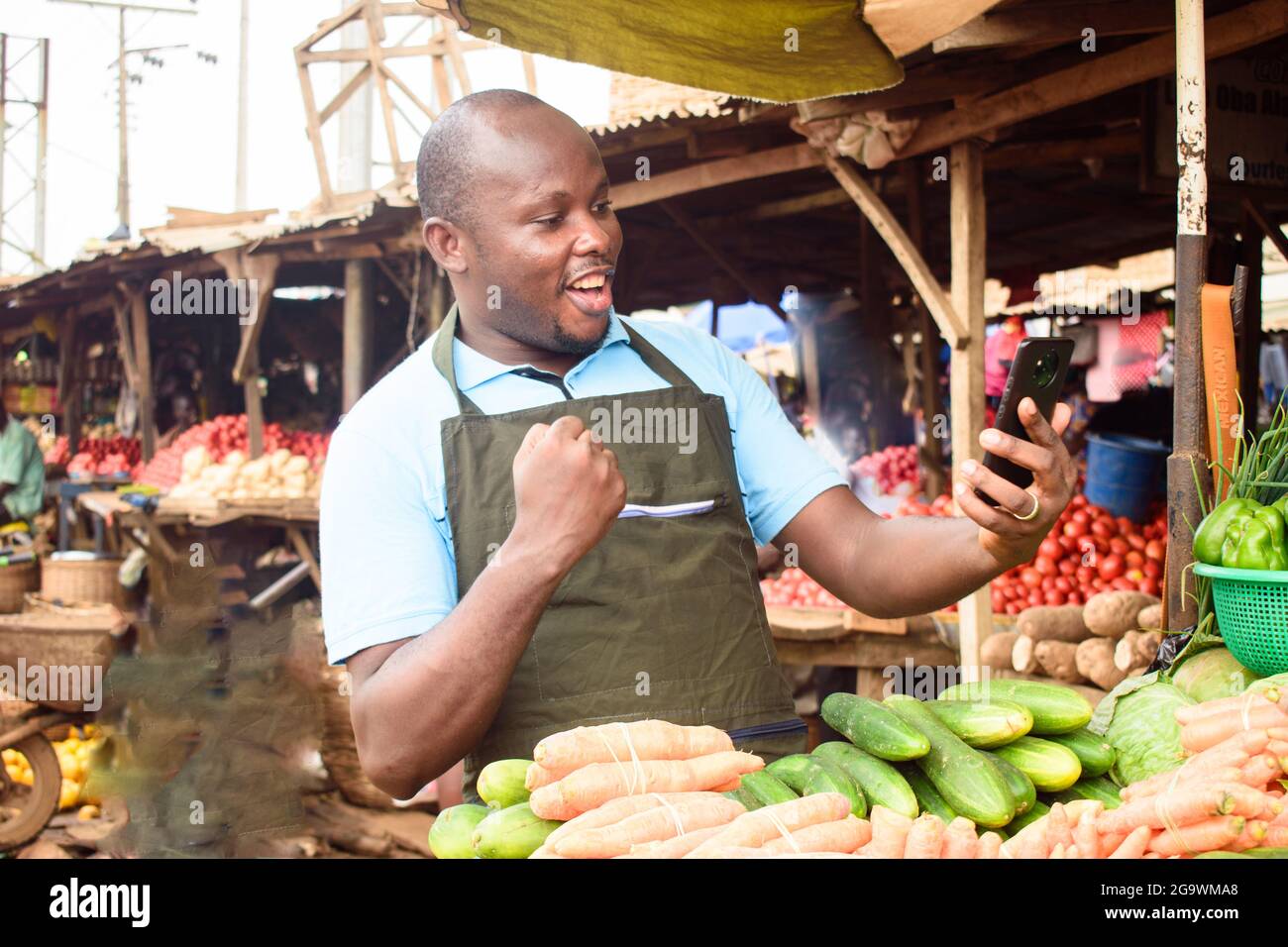 Photo de stock d'un heureux homme de vente d'épicerie africaine avec tablier et smartphone, prêt à vendre aux clients Banque D'Images