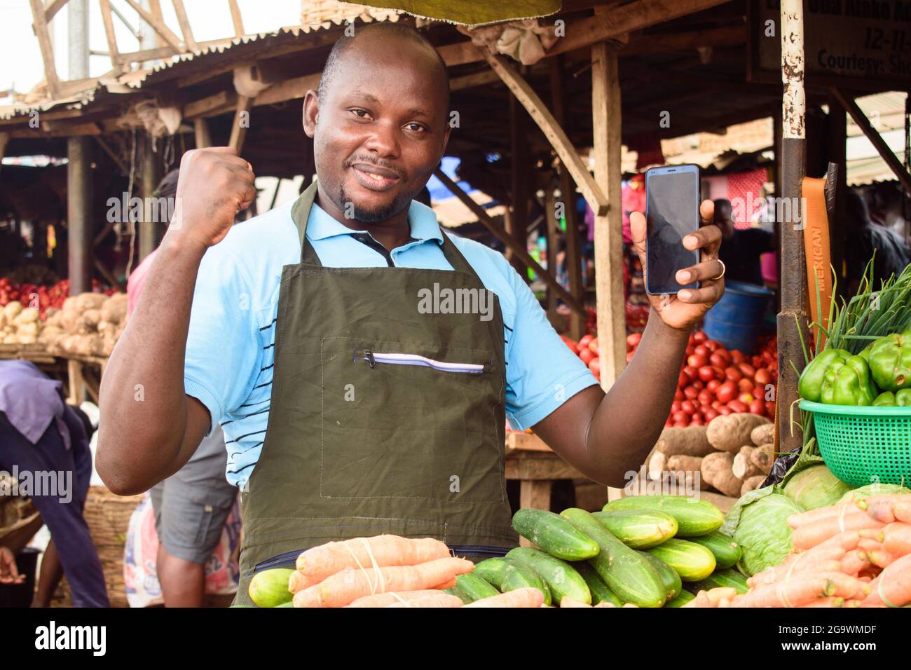 Photo de stock d'un heureux homme de vente d'épicerie africaine avec tablier et smartphone, prêt à vendre aux clients Banque D'Images