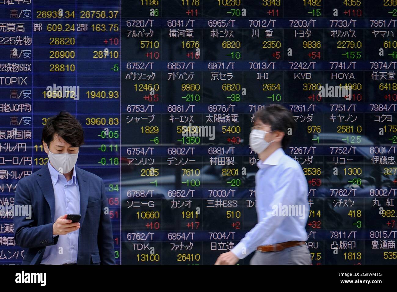 Tokyo, Japon. 24 juin 2021. Les personnes portant des masques de visage comme mesure préventive contre la propagation de Covid-19 marchent au-delà d'un écran affichant les indices de la moyenne de Nikkei et de la bourse mondiale en dehors d'une maison de courtage, dans le cadre de l'épidémie de coronavirus (COVID-19), à Tokyo. (Image de crédit : © James Matsumoto/SOPA Images via ZUMA Press Wire) Banque D'Images