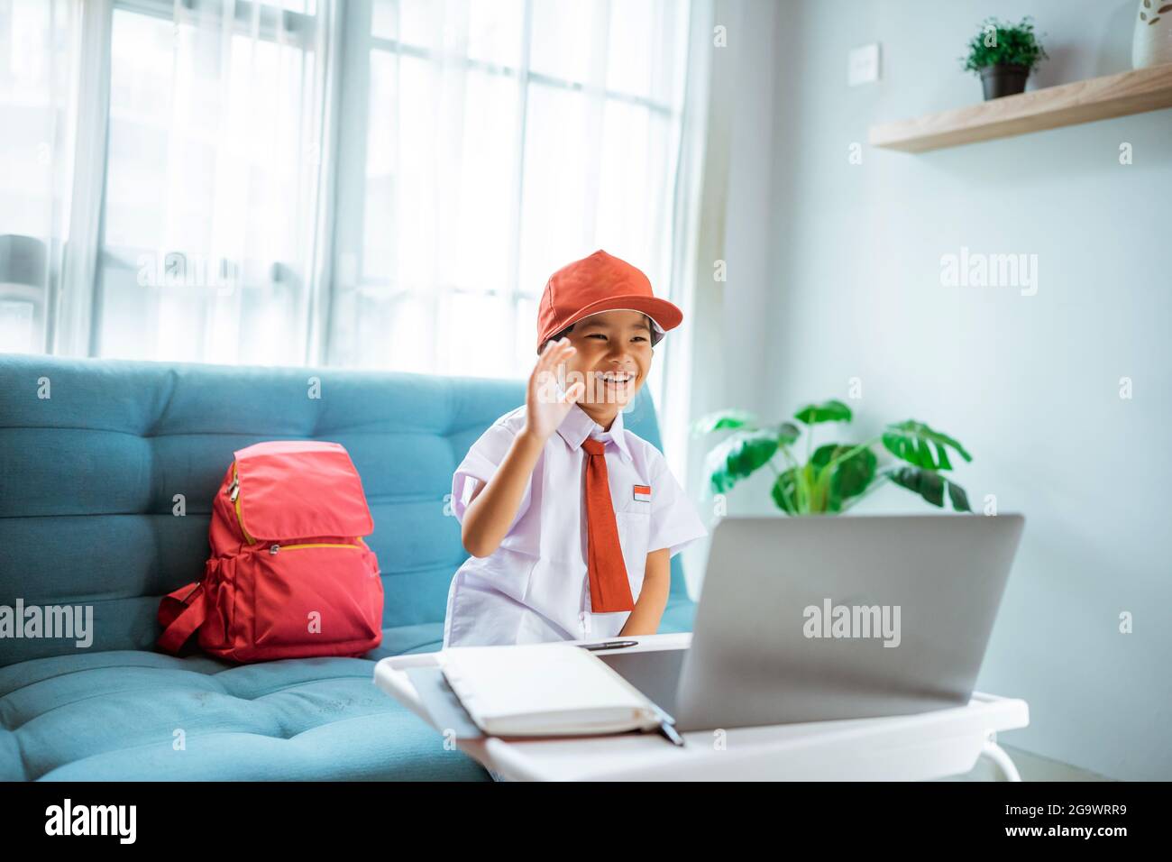 élève de l'école primaire avec uniforme agitant à son professeur et ami pendant la session de classe en ligne Banque D'Images
