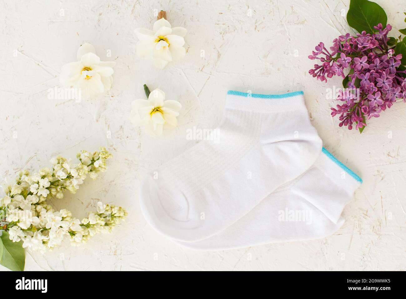 Paire de chaussettes pour femmes, fleurs de lilas, fleurs de jasmin et bourgeons de fleurs de jonquilles sur fond blanc structuré, vue du dessus. Banque D'Images