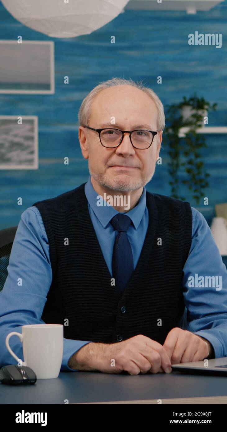 Homme d'affaires âgé et prospère, entrepreneur assis dans un espace de travail, regardant la caméra sourire. Manager senior travaillant à domicile pour les start-up, préparé pour une réunion en ligne à l'aide de gadgets moden Banque D'Images