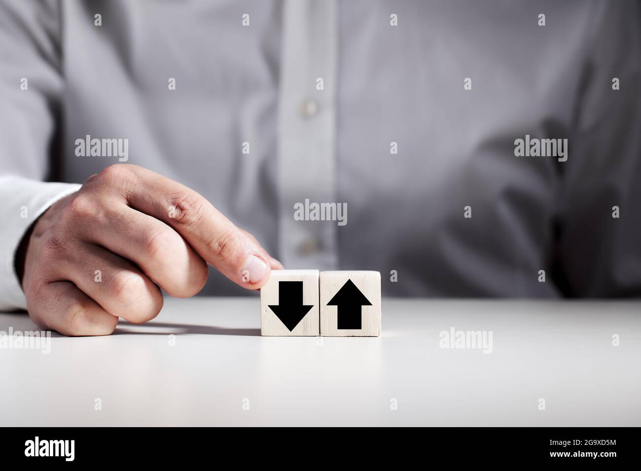 Homme d'affaires choisissant le cube en bois avec la flèche vers le bas à côté du cube avec la flèche vers le haut. Banque D'Images