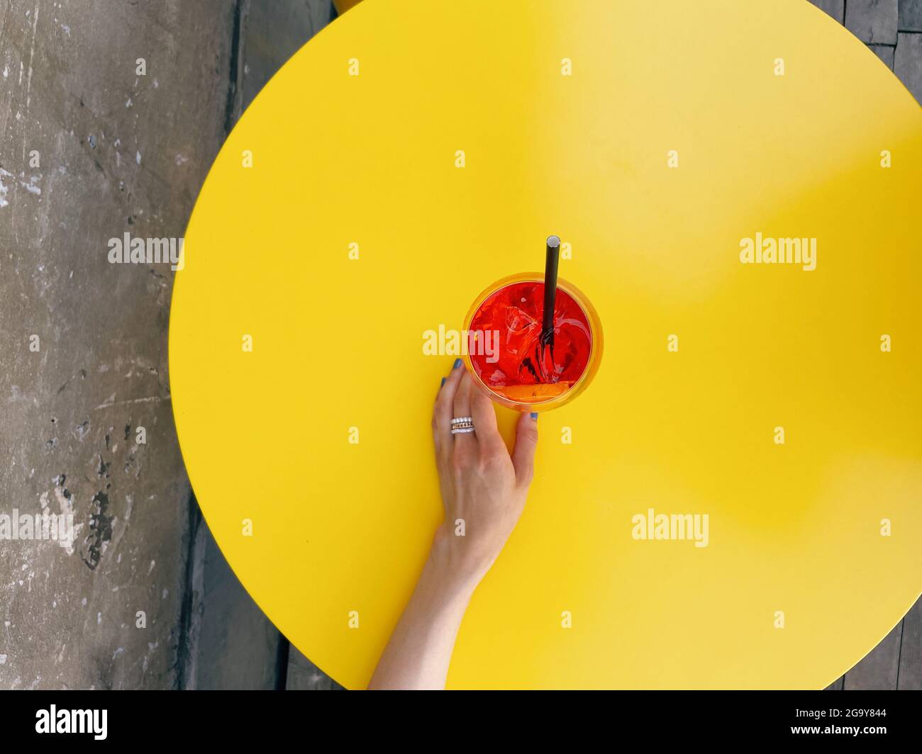 Vue en hauteur d'une femme qui se présente pour un cocktail aperol Spritz sur une table jaune Banque D'Images