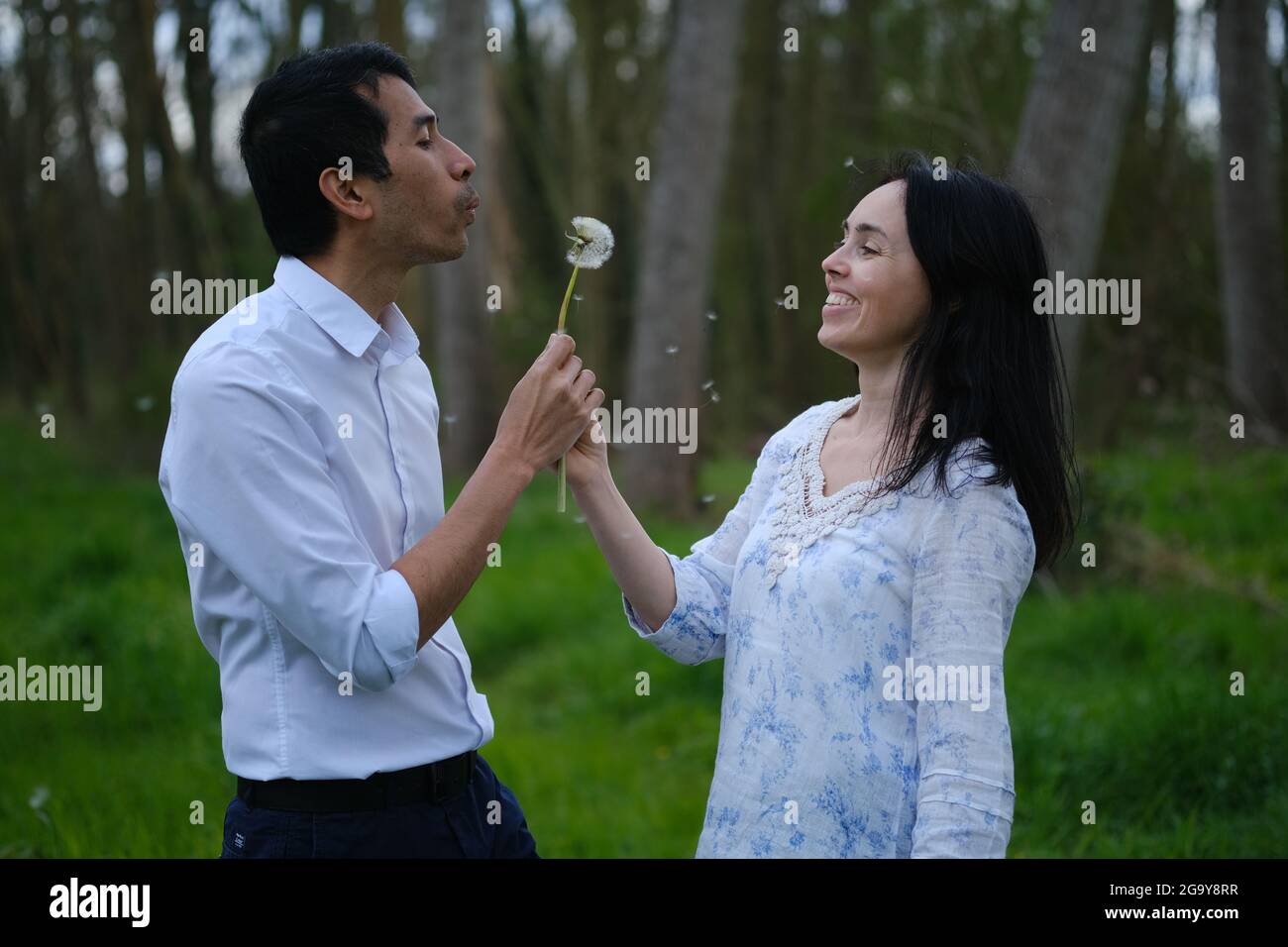 Couple debout dans un parc soufflant une horloge pissenlit, France Banque D'Images