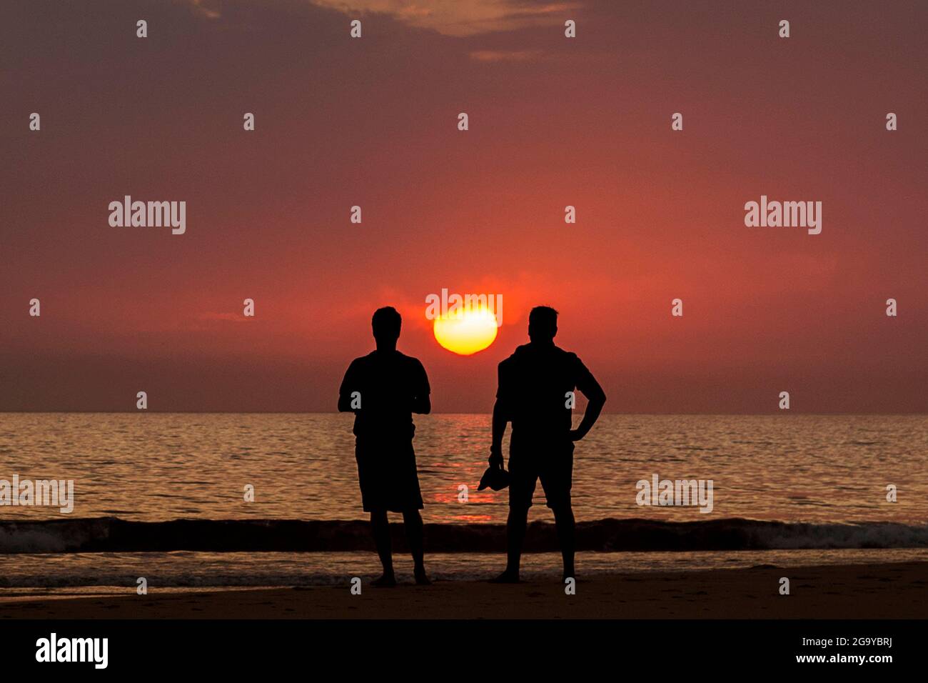 Vue arrière de deux hommes debout sur la plage au coucher du soleil, plage de Los Lances, Tarifa, Cadix, Andalousie, Espagne Banque D'Images