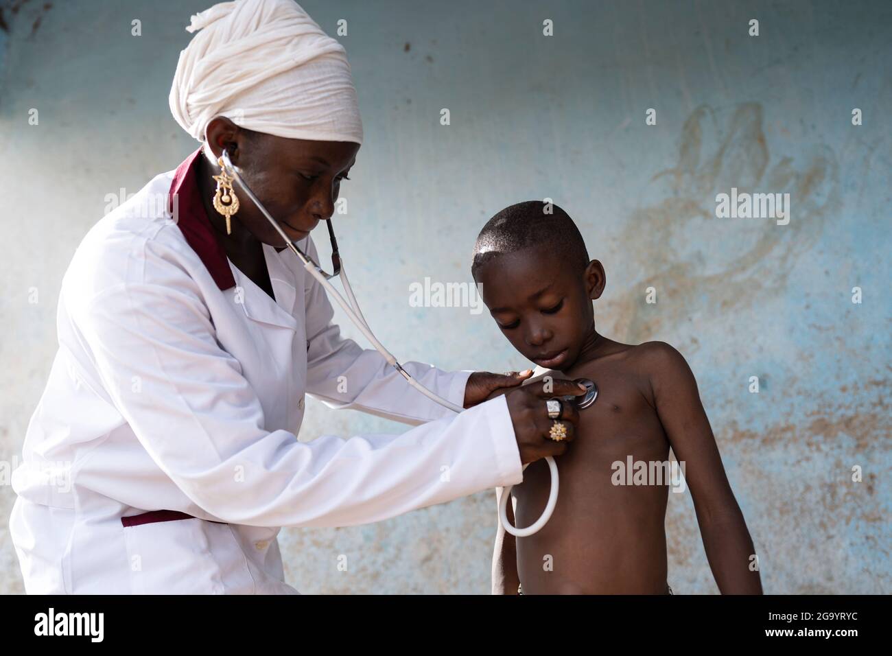 Infirmière noire dans un uniforme blanc ausculting un petit garçon africain nu attentif poitrine avec un stéthoscope lors d'une visite de routine pour vérifier pour abn Banque D'Images