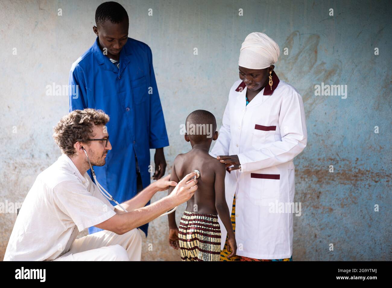 Dans cette image, un volontaire médical caucasien auscultation les poumons d'un petit garçon africain maigre sous la supervision du responsable pediatr Banque D'Images