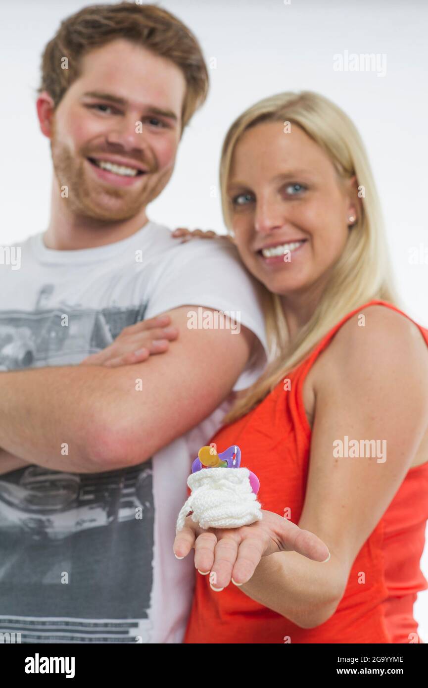 Heureux couple tenant fièrement un bébé bootee avec une sucette à l'appareil photo , Allemagne Banque D'Images