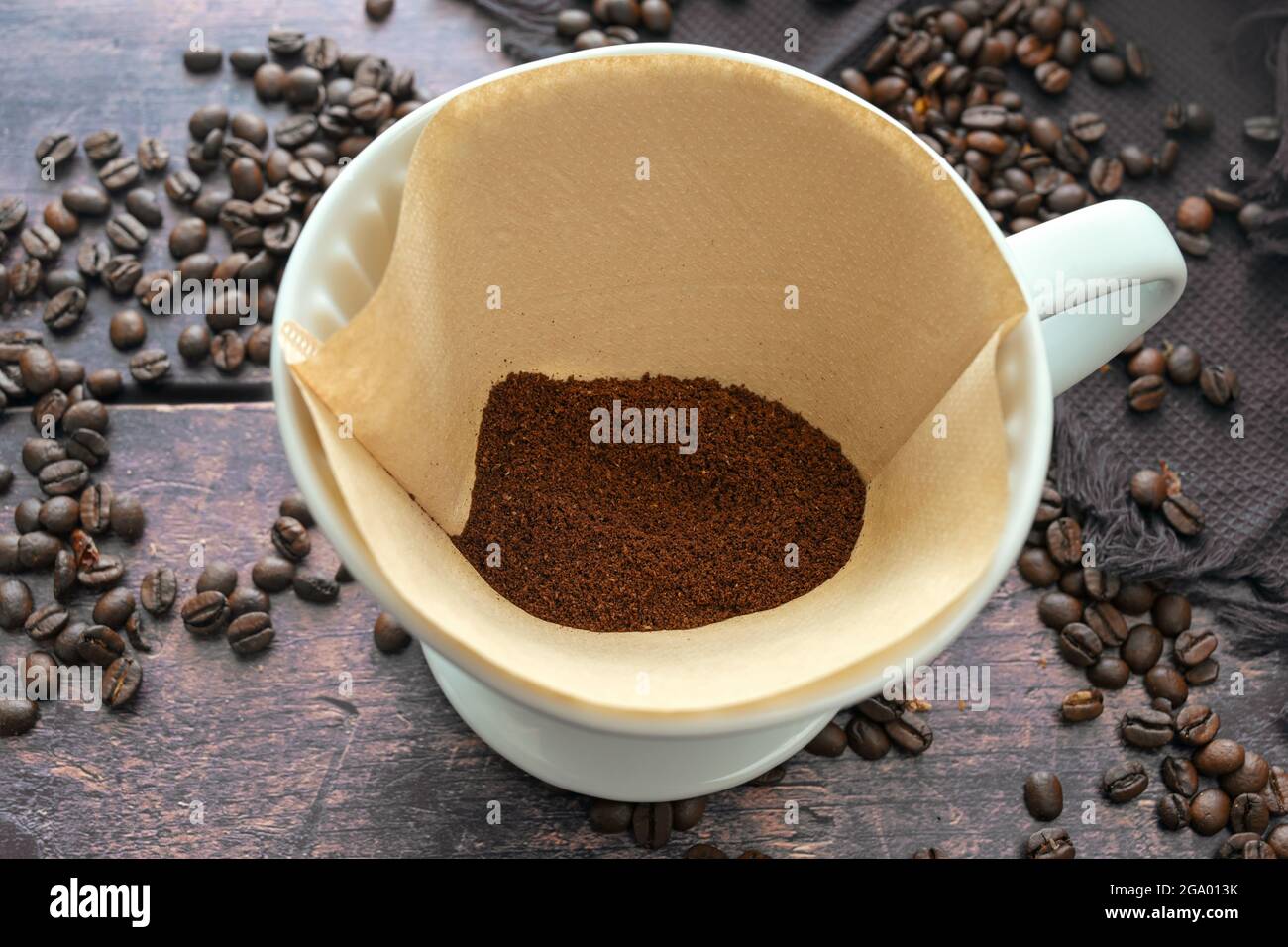 Café moulu dans un sac de filtre en papier et dans un support en porcelaine pour une boisson chaude infusé aromatique, table en bois rustique avec quelques grains, foc sélectionné Banque D'Images