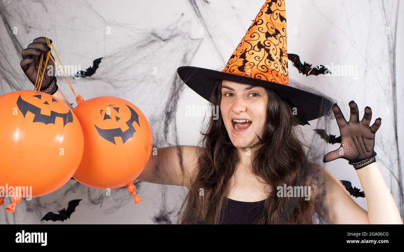Une femme en costume de sorcière dans un chapeau et des gants à l'arrière-plan avec des chauves-souris tient des balles de citrouille et dit boo. Bannière longue pour Halloween. Banque D'Images