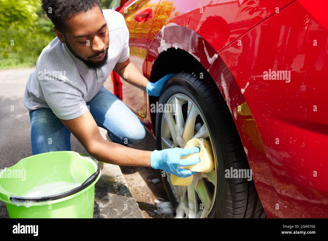 Homme lavant les roues de la voiture pendant le service de voiturier en utilisant le seau et l'éponge Banque D'Images