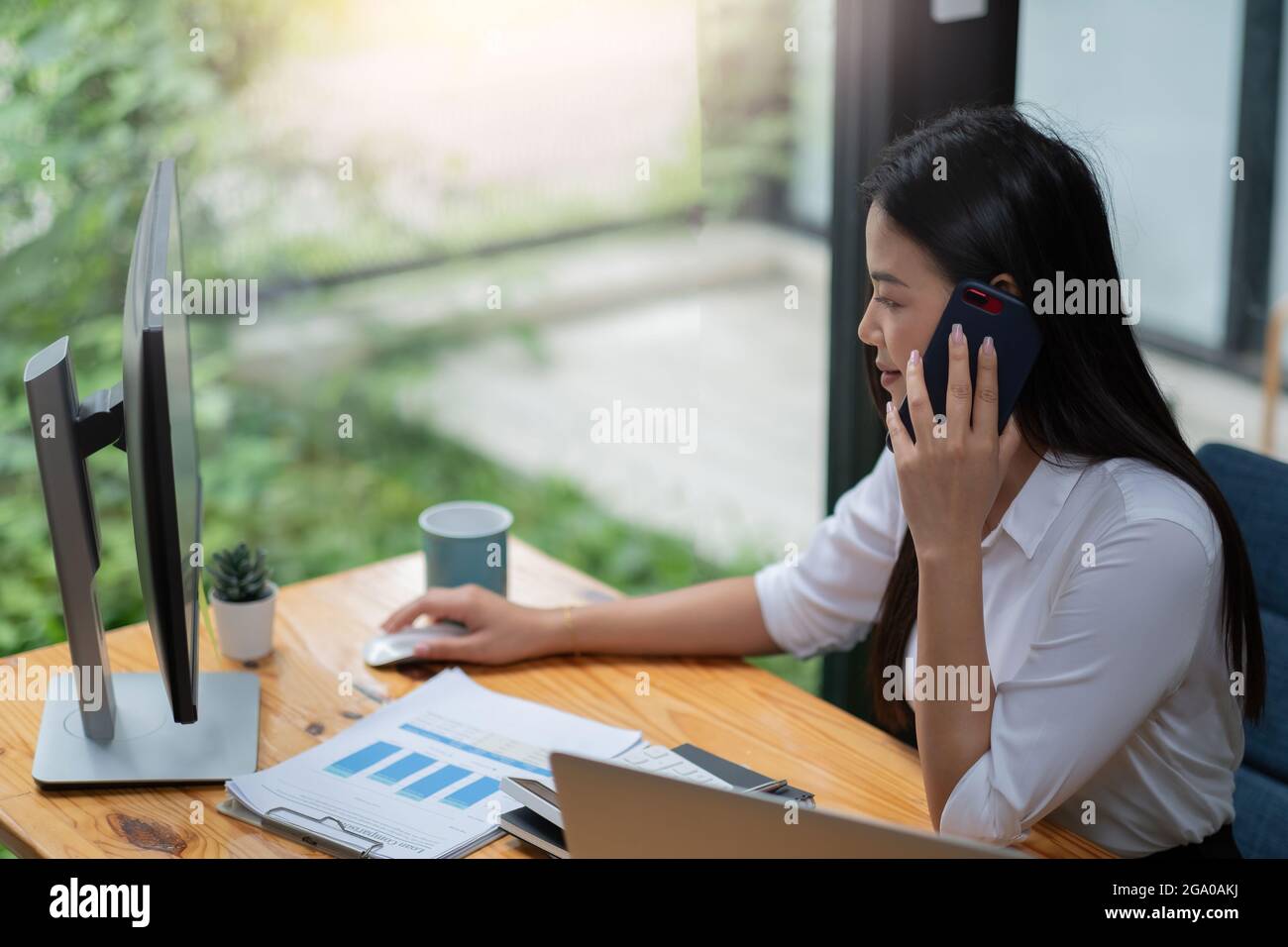 Jeune femme asiatique travaillant sur un ordinateur portable au bureau tout en parlant au téléphone, concept financier d'entreprise Banque D'Images