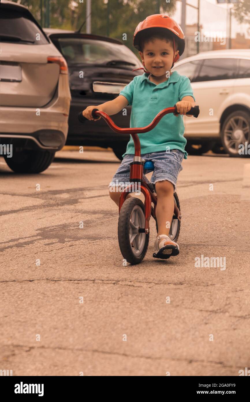 preschooler souriant et apprenant à monter à vélo avec un casque tout en roulant autour des voitures concept danger de la route Banque D'Images