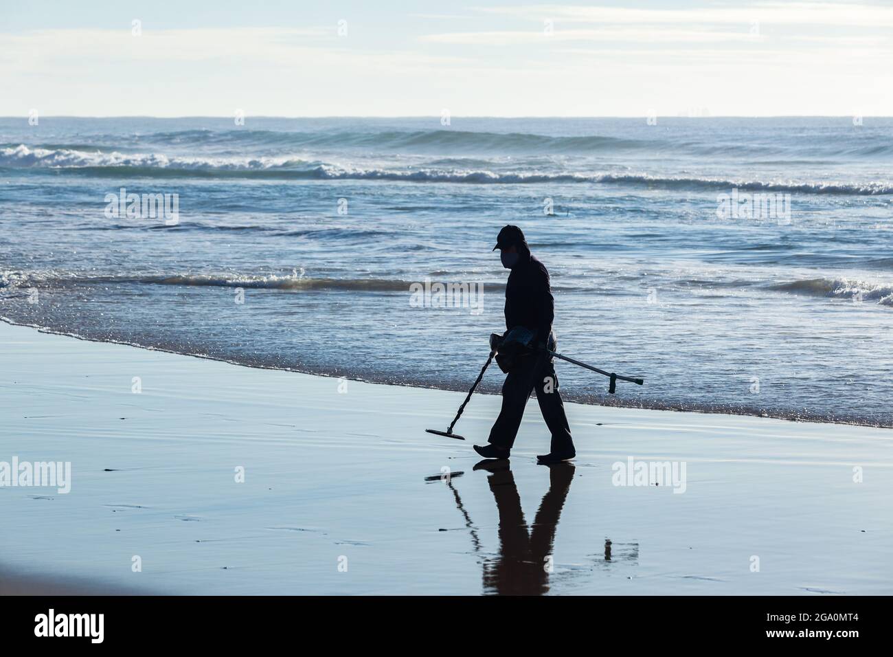 Chasseur de trésors homme non reconnaissable silhoueté marchant sur la plage vagues de l'océan ligne de l'eau avec détecteur de métal à la recherche de trésors perdus. Banque D'Images