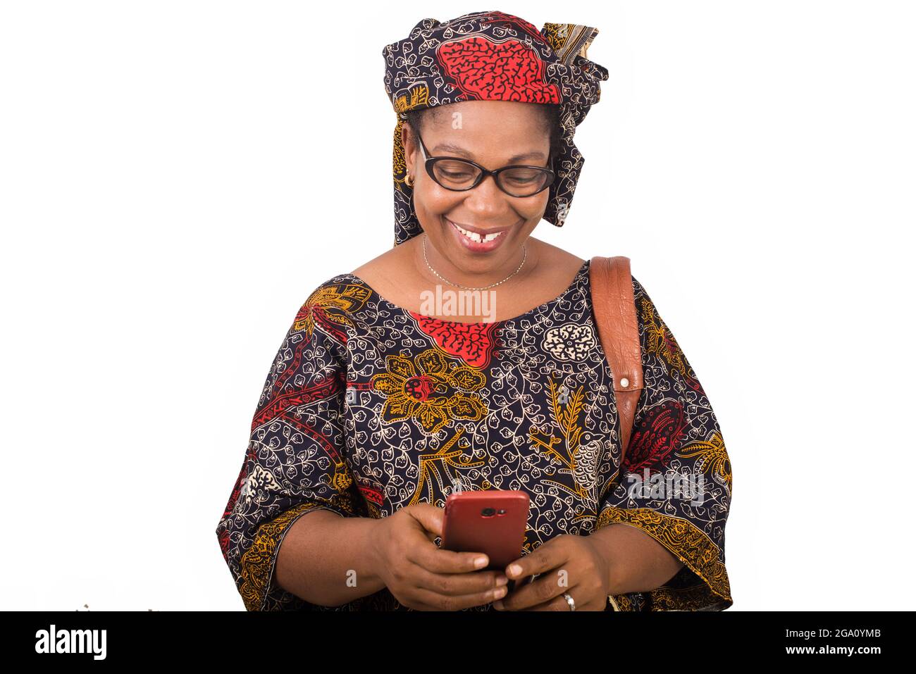 femme africaine mûre en toile de longe debout sur fond blanc regardant le téléphone mobile tout en souriant. Banque D'Images