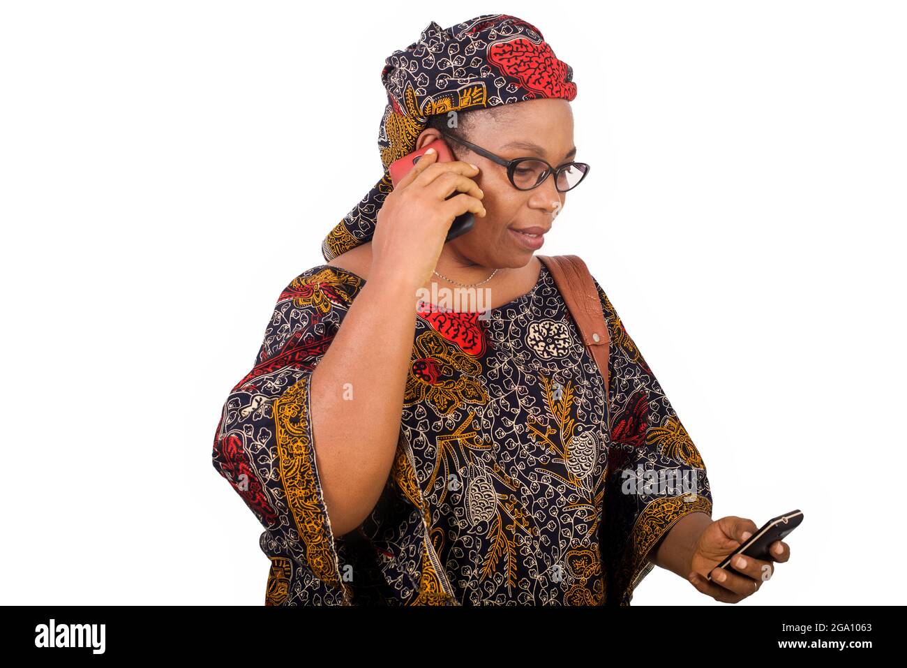 femme africaine mûre en toile de longe sur fond blanc communiquant avec le téléphone mobile tout en souriant. Banque D'Images