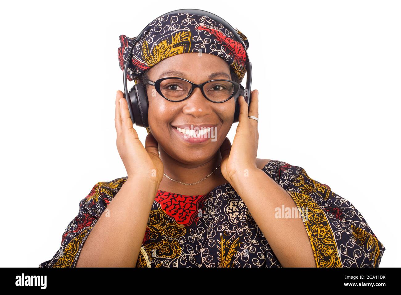 femme africaine mûre souriante en tissu de longe et foulard africain écoutant de la musique avec des écouteurs sur fond blanc Banque D'Images