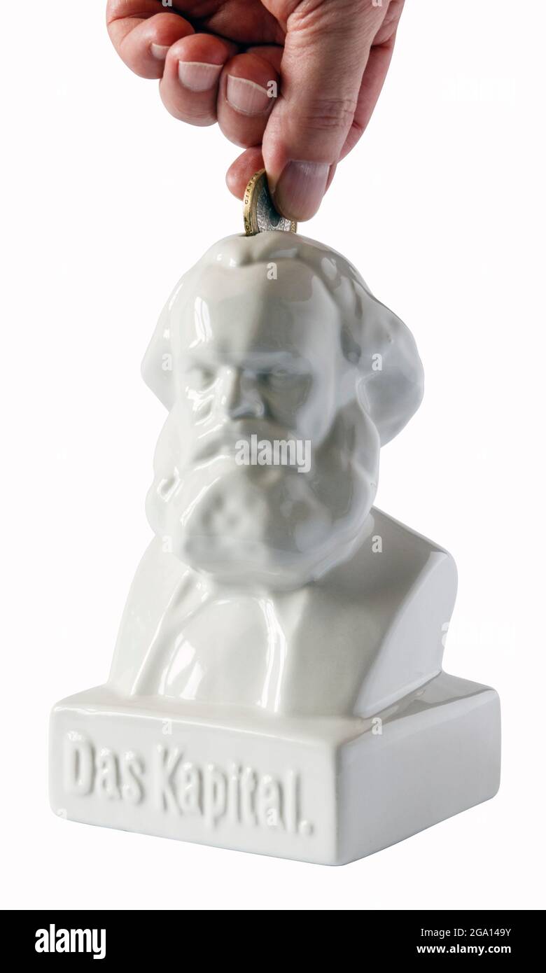 Main masculine insérant une pièce de monnaie d'une livre dans une boîte d'argent en céramique blanche sous la forme d'un buste du philosophe allemand Karl Marx, intitulé « Das Kapital » Banque D'Images
