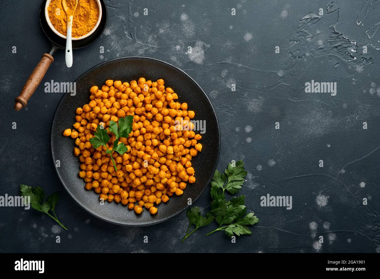 Pois chiches frits au curcuma avec persil et citron vert dans une assiette noire sur un fond de table noir ancien. Pois chiches épicés grillés ou chana ou chole indien, Banque D'Images