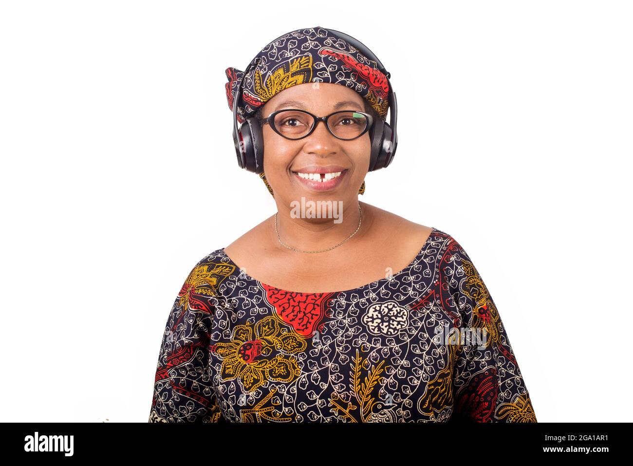 femme africaine mûre souriante en tissu de longe et foulard africain écoutant de la musique avec des écouteurs sur fond blanc Banque D'Images