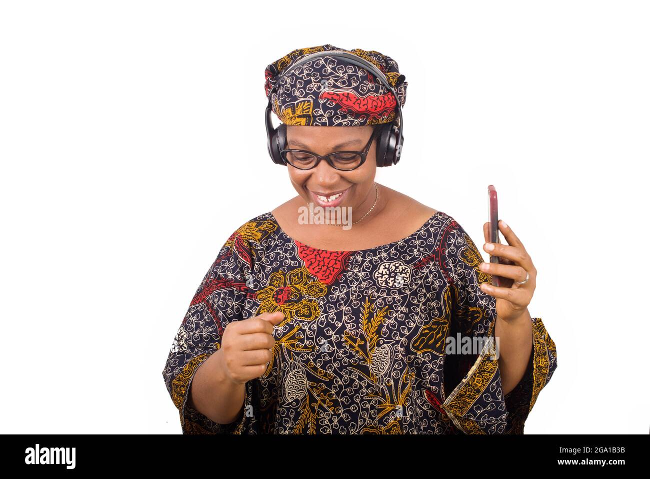 femme africaine mûre en loincloth écoutant de la musique à l'aide d'écouteurs et de téléphone portable ayant le geste de la main Banque D'Images