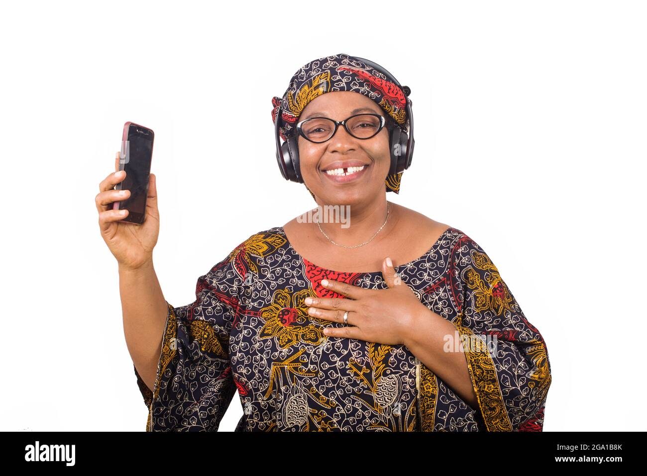 femme africaine mûre en loincloth écoutant de la musique à l'aide d'écouteurs et de téléphone portable ayant le geste de la main Banque D'Images