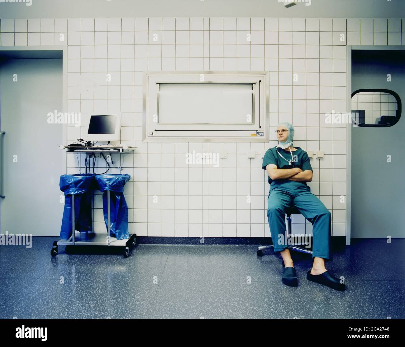 Le chirurgien est assis dans des exfoliants et un capuchon chirurgical à l'extérieur d'une salle d'opération; Allemagne Banque D'Images