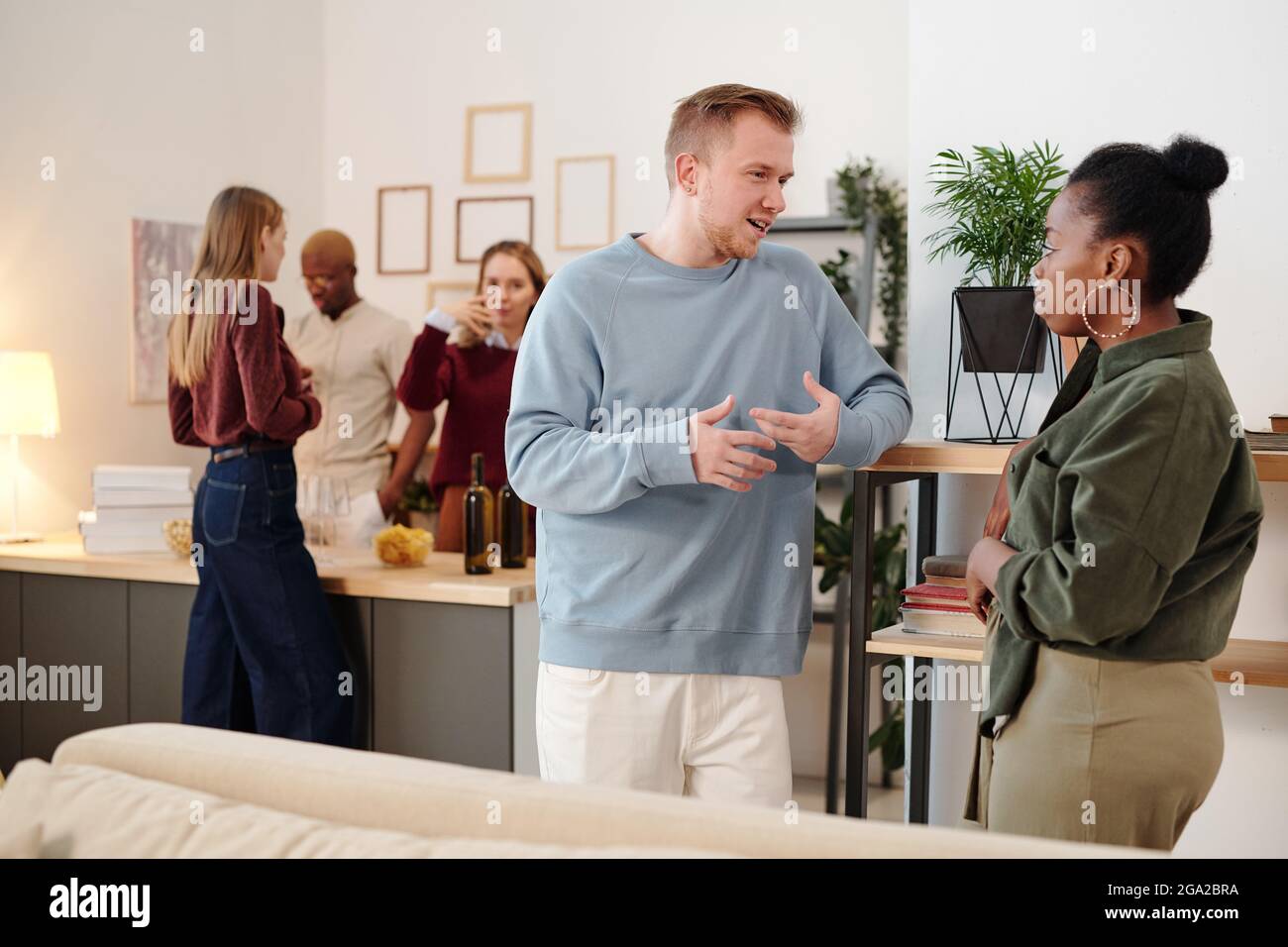 Joyeux jeune couple affectueux avec des bouteilles de bière regarder vous avez le sourire tout en profitant de la fête à la maison contre le chat amis Banque D'Images
