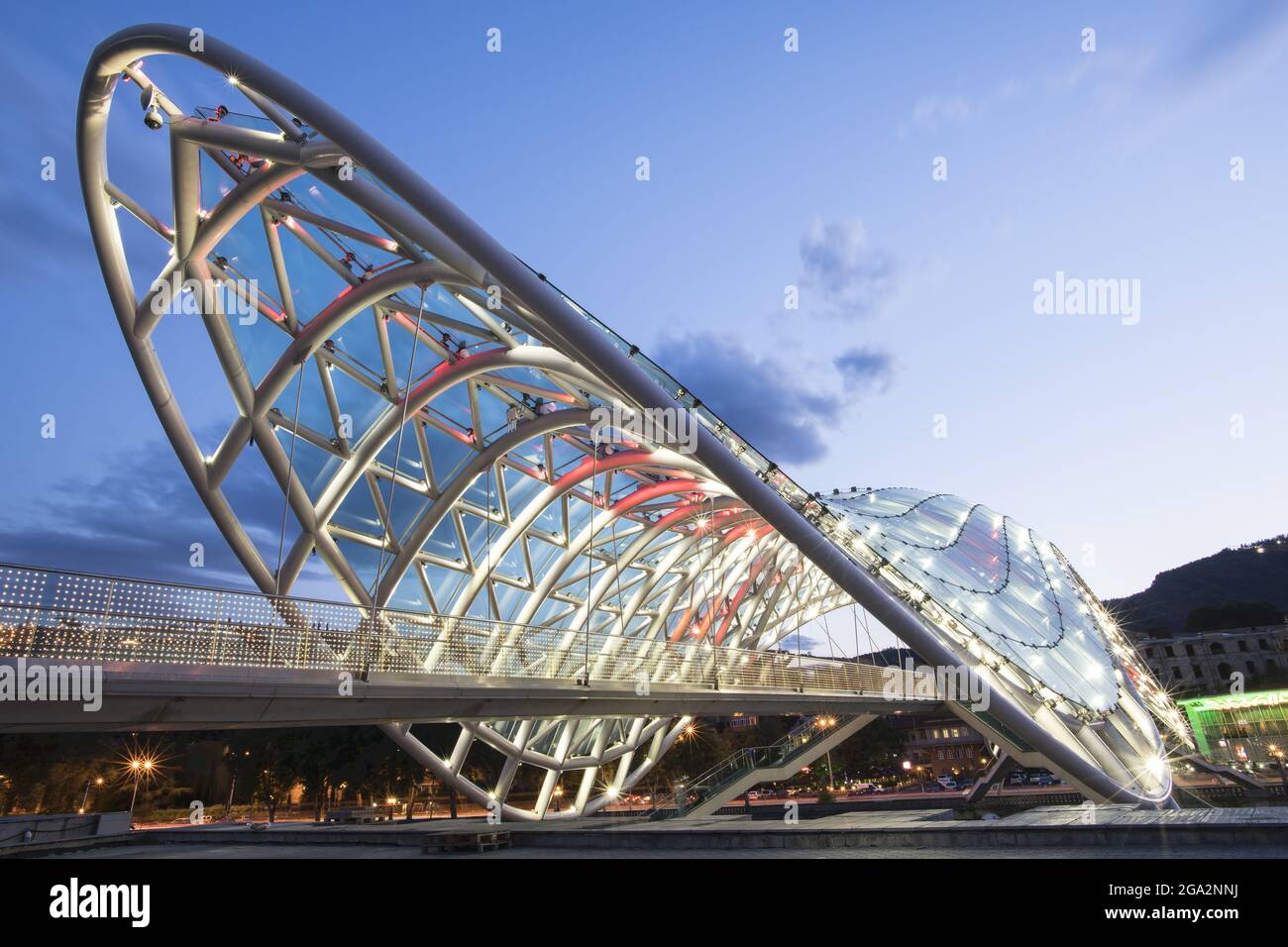 Le pont piétonnier en forme d'arc de la paix, illuminé au crépuscule, enjambant la rivière Mtkvari (Kura) reliant le parc Rike et le vieux Tbilissi Banque D'Images