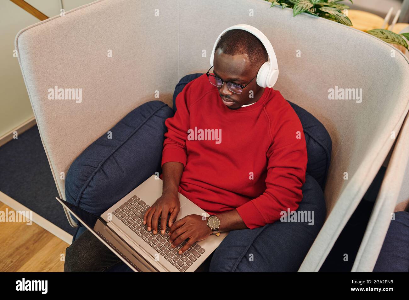 Jeune directeur de bureau ou designer africain de casque à la recherche à l'affichage de l'ordinateur portable sur ses genoux lors de la préparation de la présentation Banque D'Images