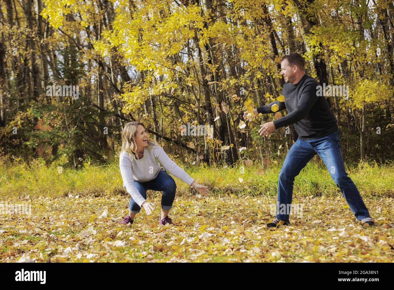 Un couple mature et marié qui passe du temps ensemble dans un parc de la ville pendant la saison d'automne, s'amusant à jeter des feuilles mortes les unes contre les autres Banque D'Images