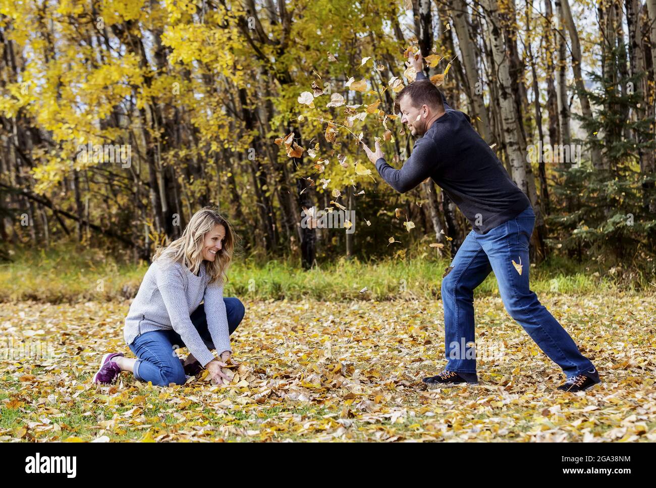 Un couple mature et marié qui passe du temps ensemble dans un parc de la ville pendant la saison d'automne, s'amusant à jeter des feuilles mortes les unes contre les autres Banque D'Images