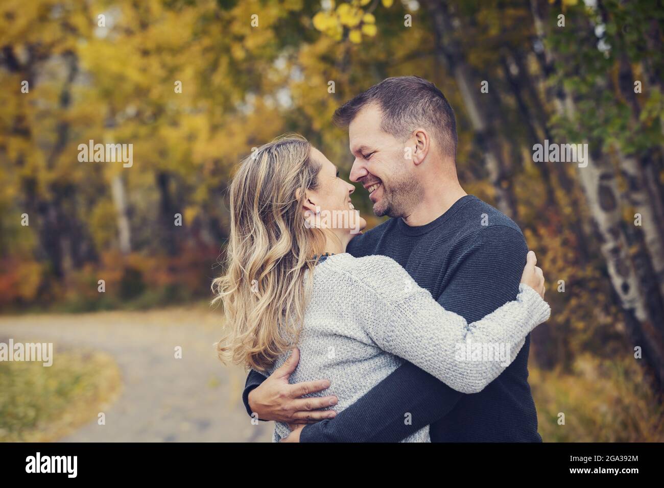 Un couple marié dans une étreinte tout en passant du temps de qualité ensemble à l'extérieur dans un parc de la ville pendant un après-midi d'automne chaud; St. Albert, Alberta, Canada Banque D'Images