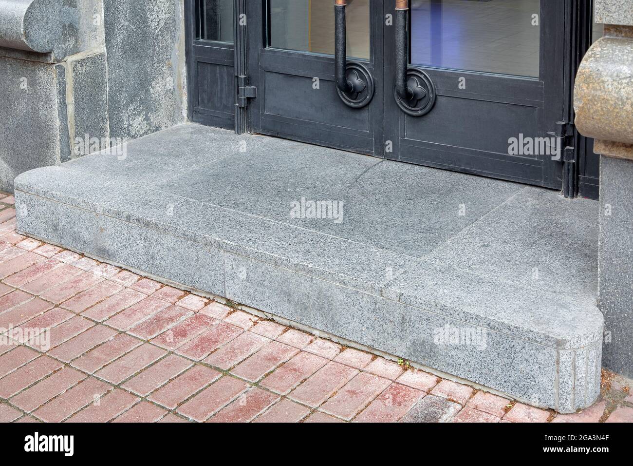 un seuil avec une porte à l'entrée du seuil du magasin avec une porte en  fer noir avec insert en verre dans le carrelage de la porte avec un clos en  granit
