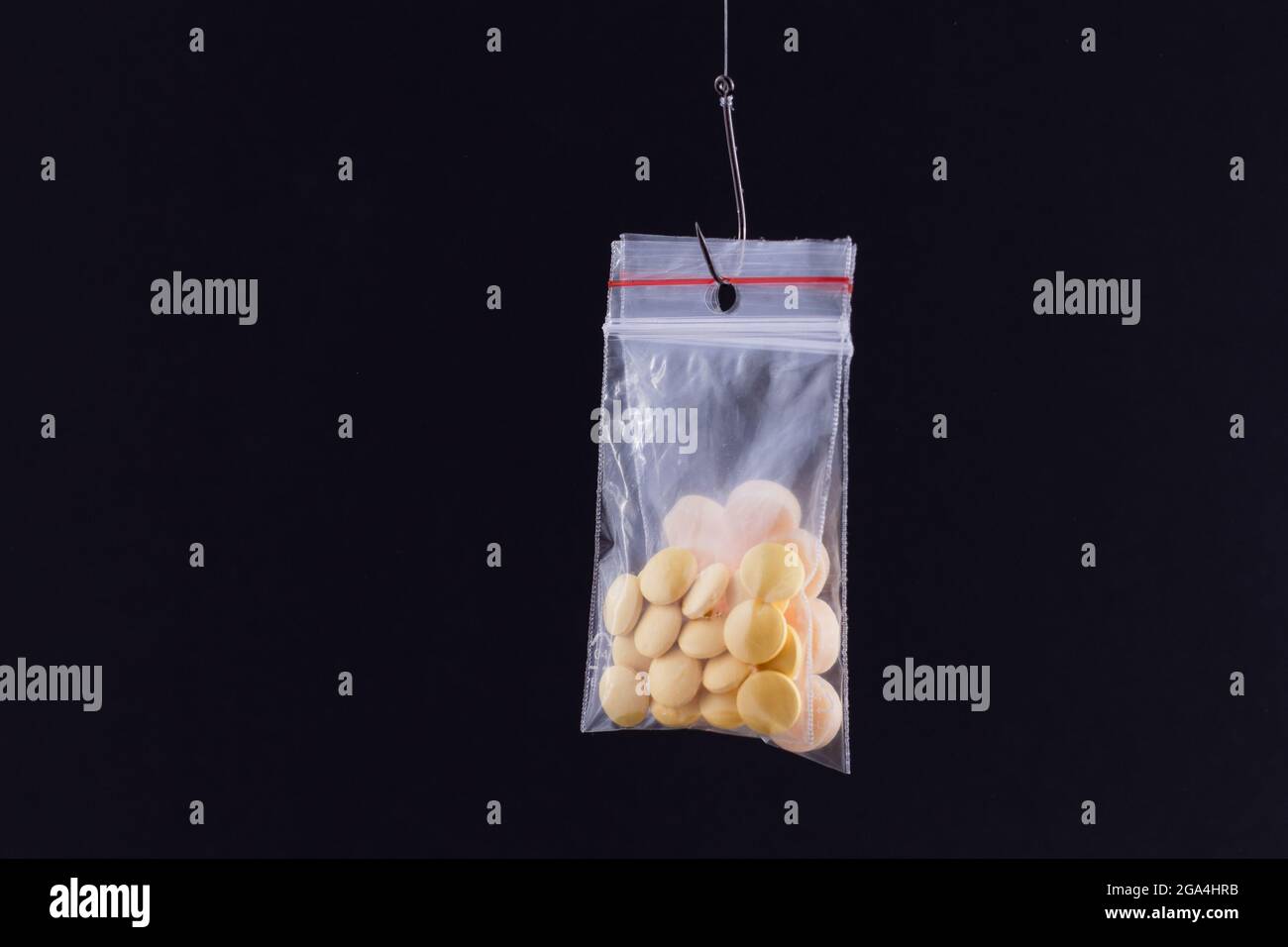 Le piège pharmaceutique et la toxicomanie - pilules colorées ou comprimés suspendus dans un petit sac Ziplock sur un crochet de pêche contre le fond noir Banque D'Images