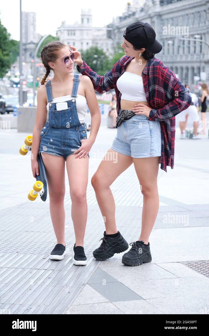 Deux femmes sympa souriant et regardant l'une à l'autre avec un skateboard. Deux amies qui se posent dans la rue. Banque D'Images
