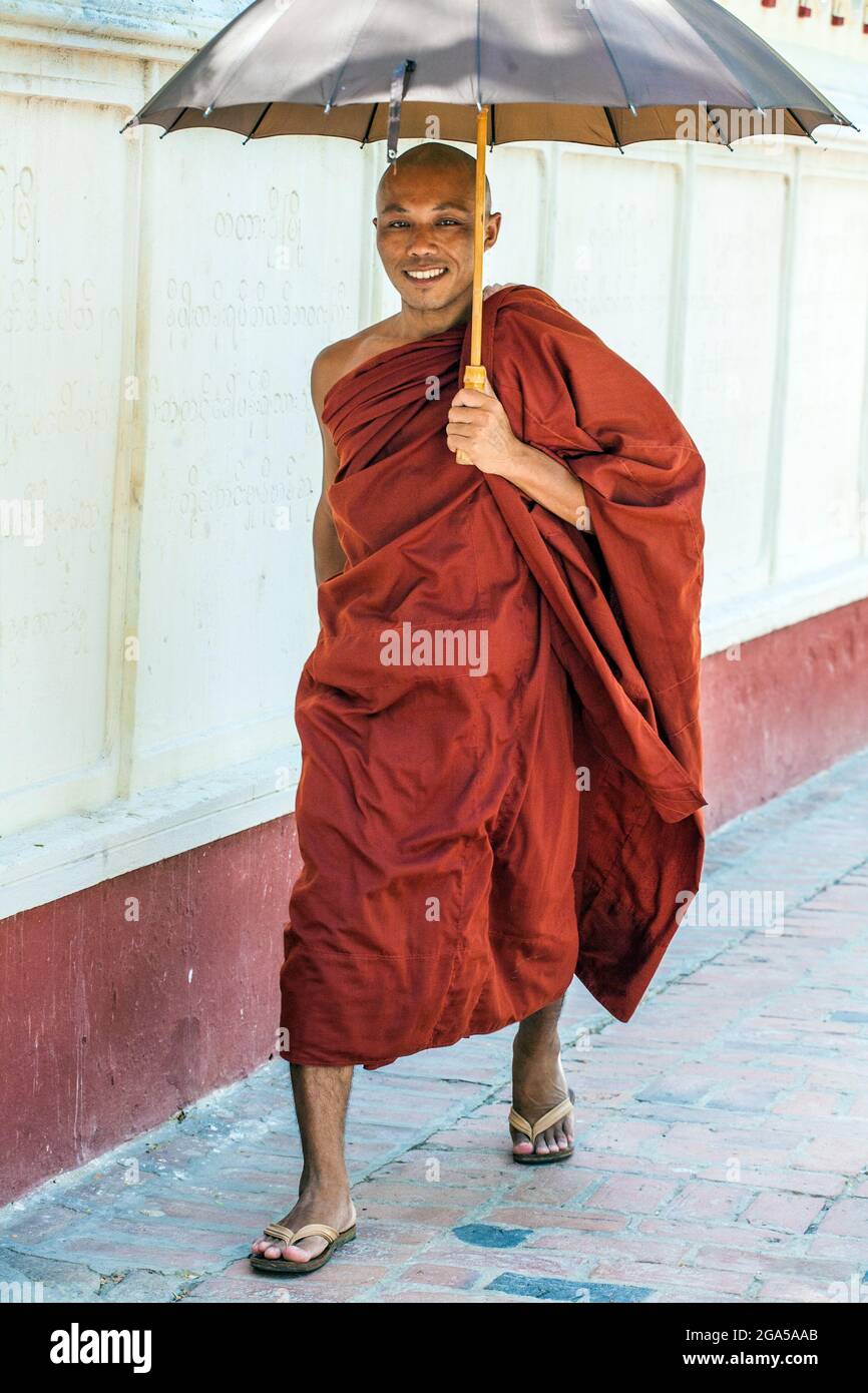 Beau moine birman souriant portant des robes de marron portant des foulées de parapluie volontairement le long du trottoir, Mandalay, Myanmar Banque D'Images