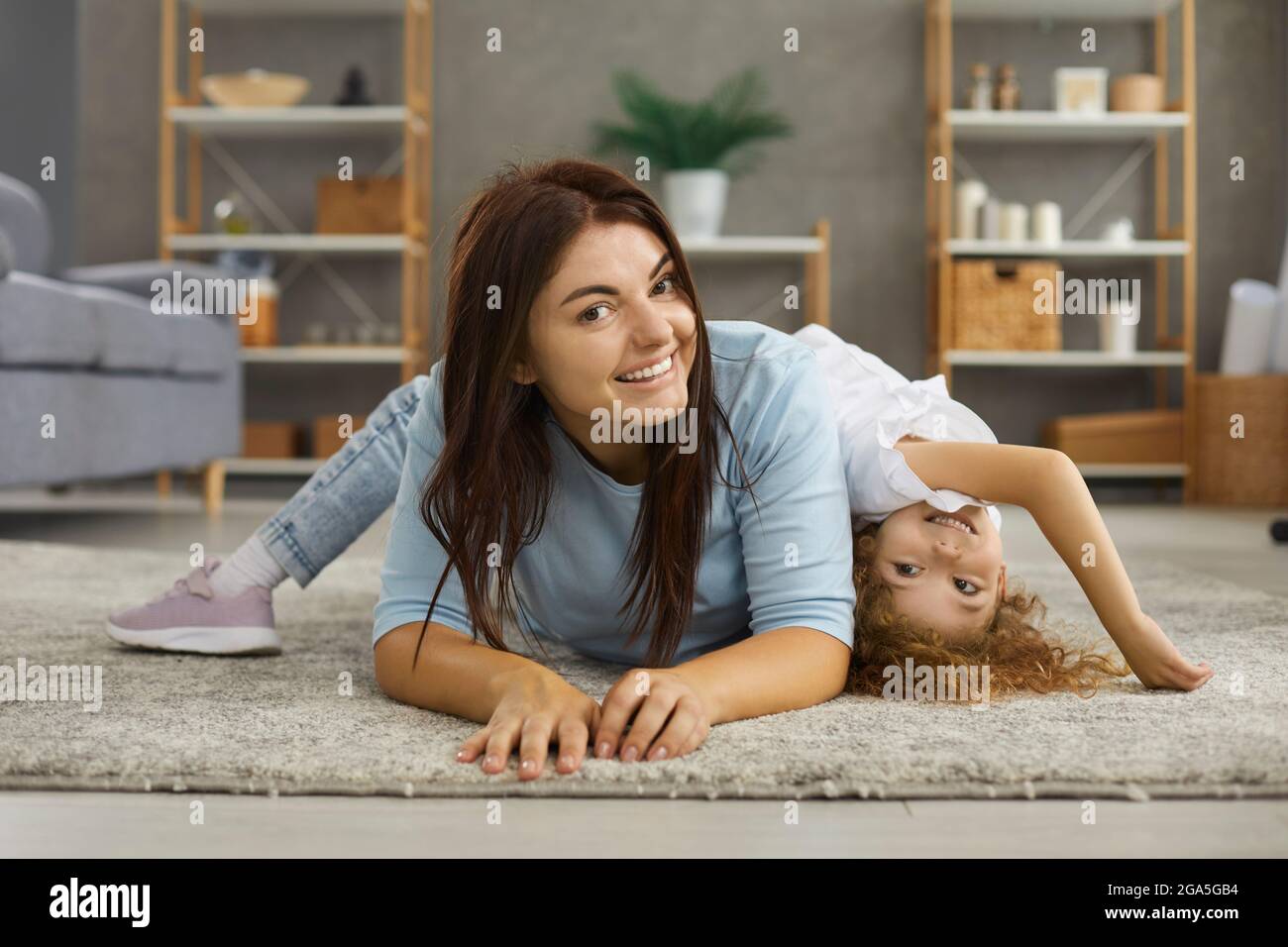 Bonne mère souriante et petite fille jouant sur un tapis chaud dans le salon Banque D'Images