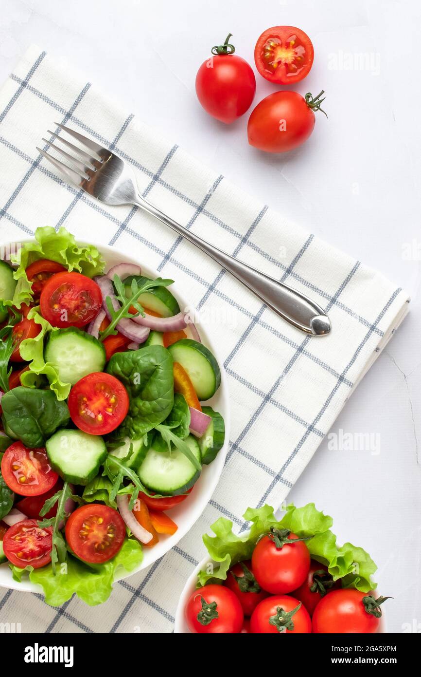 Légumes sur une plaque blanche sur fond de marbre gris. Vue de dessus. Salade faite de tomates cerises, concombres, arugula, basilic et garnie d'olive Banque D'Images