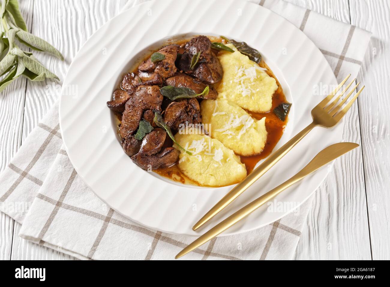 Foies de poulet avec Sage servis avec polenta sur une plaque blanche sur une table en bois clair, Fegatini di pollo alla salvia, cuisine italienne Banque D'Images