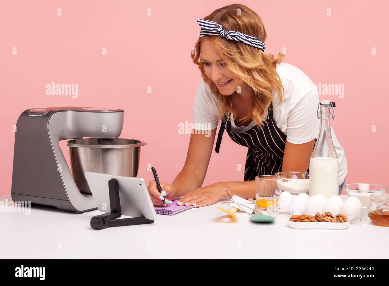 Jeune adulte concentré femelle se préparer à faire de la boulangerie, écrire de nouvelles recettes d'Internet, en utilisant la tablette numérique, préparer des gâteaux. Salle de studi Banque D'Images