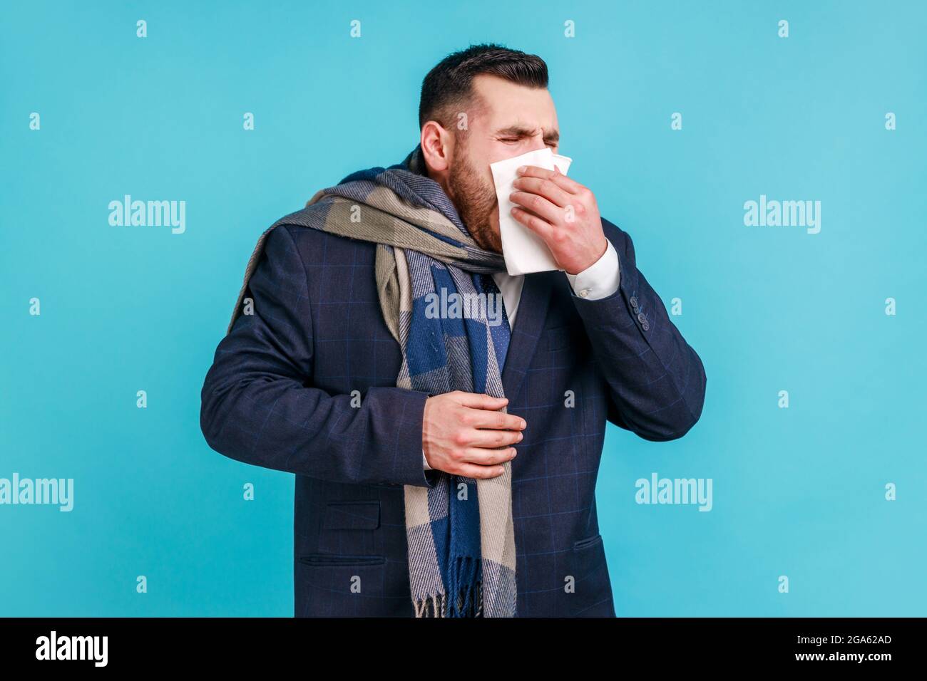 Rhume et grippe. Portrait d'un jeune homme d'affaires barbu malade en costume élégant debout, tenant le tissu sur la bouche et le nez, enveloppé dans une écharpe chaude. Indo Banque D'Images
