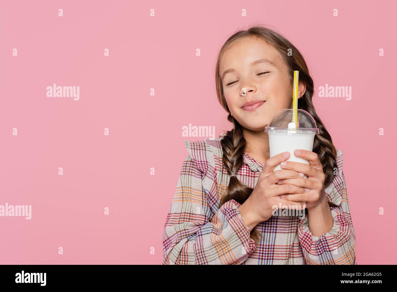 Heureuse préadolescence fille avec les yeux fermés tenant Milkshake isolé sur rose Banque D'Images