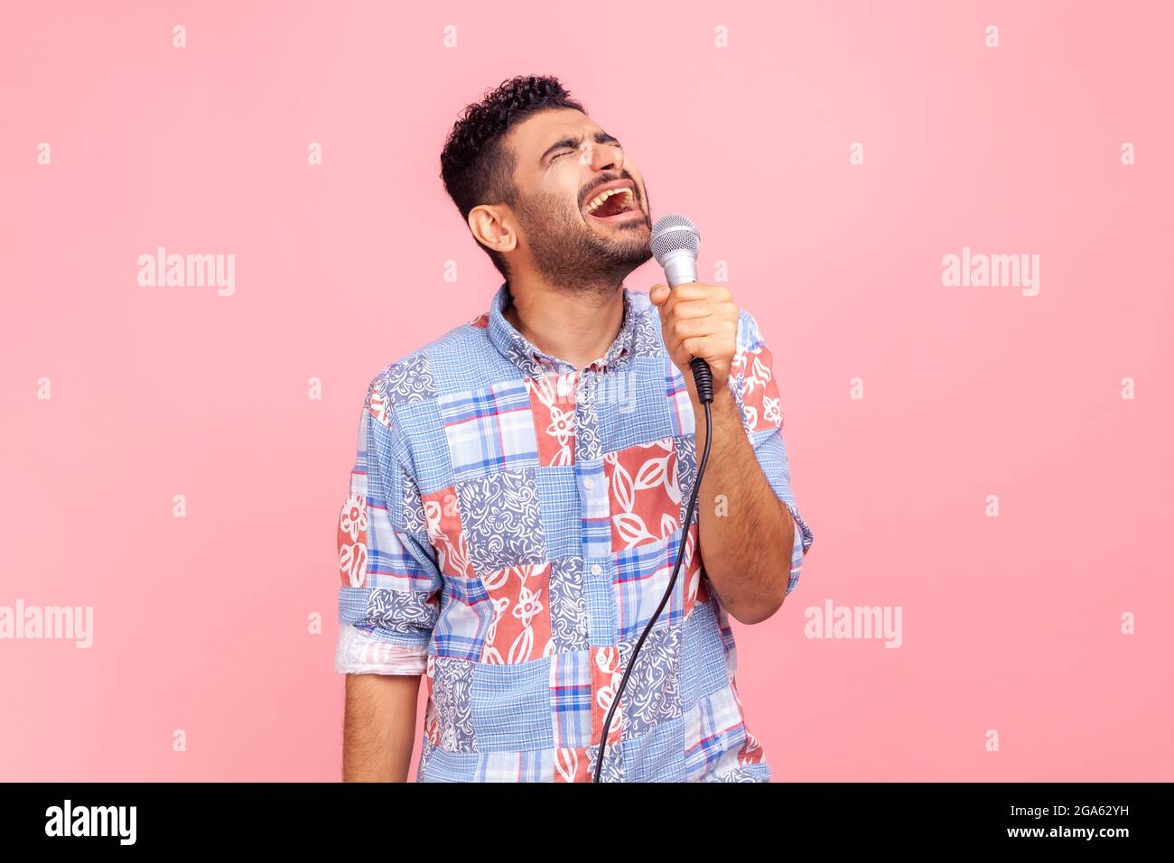 Homme positif et enthousiaste avec une barbe dans une chemise bleue décontractée chantant des chansons, tenant un microphone, chanteur faisant des performances, garde les yeux fermés. Salle de studio intérieure Banque D'Images