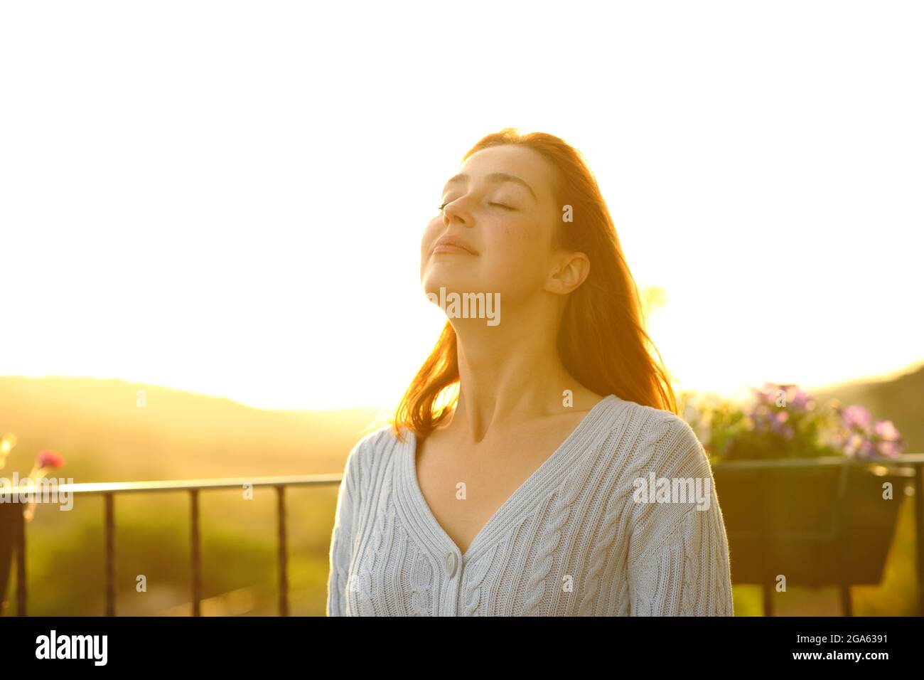 Une femme satisfaite respire de l'air frais dans un balcon à la maison au coucher du soleil Banque D'Images