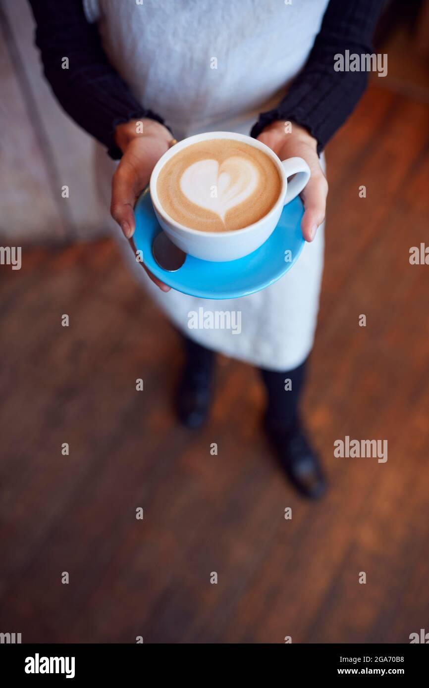 Gros plan de la serveuse au café-restaurant tenant une tasse avec coeur Design versé dans le lait Banque D'Images